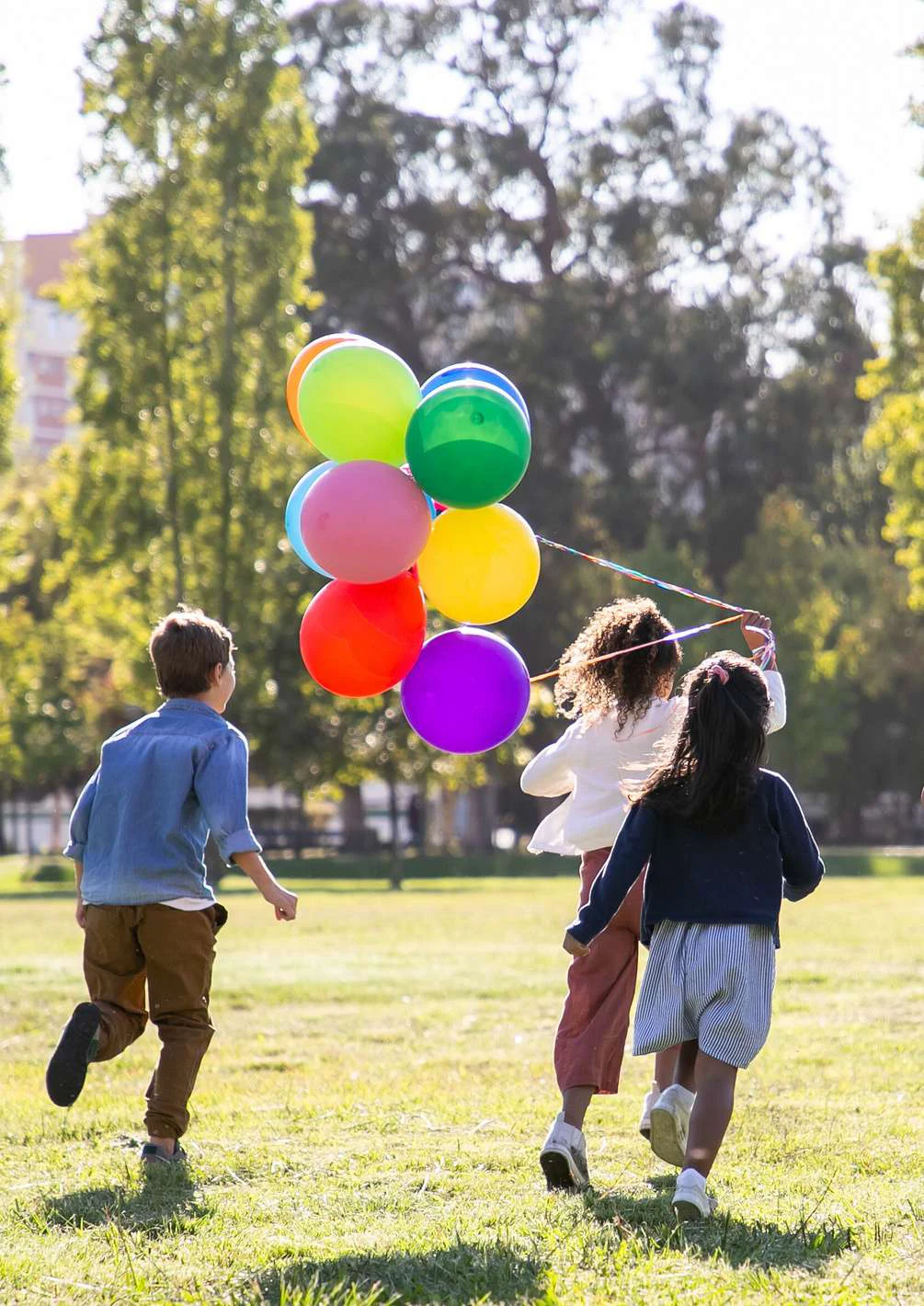 Crianças a correr num parque com balões coloridos
